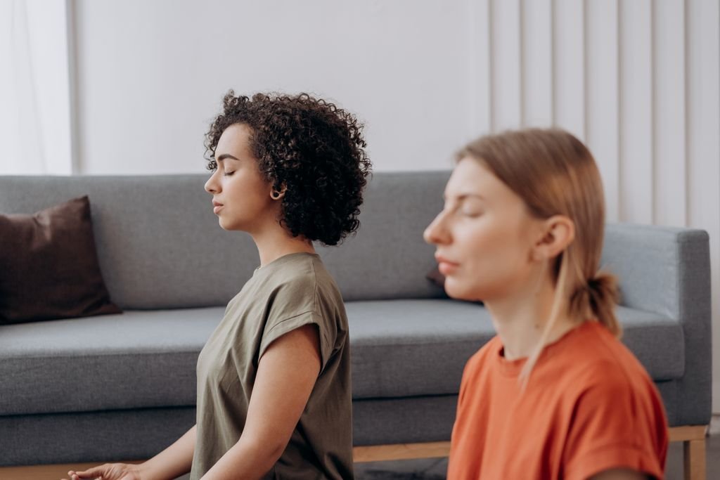 Two women practicing meditation in a serene indoor setting, fostering mindfulness.